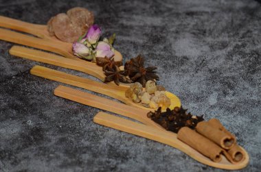 Sağlıklı bitki ve baharat çeşitleri (Tarçın, Acacia, Frankincense, Anise yıldızı) karanlık bir arka planda izole edilmiş tahta kaşıklarda bulunur..