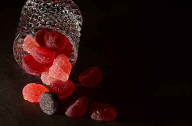 Siyah bir zemin üzerinde izole edilmiş cam şeker kavanozundan çıkan lezzetli jöle şekerlemelerden oluşan bir çekim..