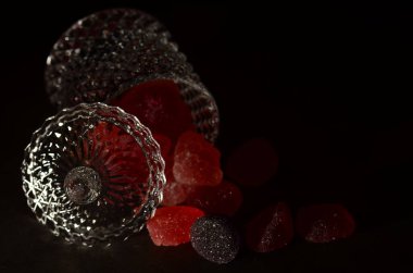 Siyah bir zemin üzerinde izole edilmiş cam şeker kavanozundan çıkan lezzetli jöle şekerlemelerden oluşan bir çekim..