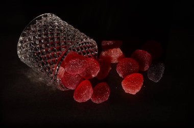Siyah bir zemin üzerinde izole edilmiş cam şeker kavanozundan çıkan lezzetli jöle şekerlemelerden oluşan bir çekim..