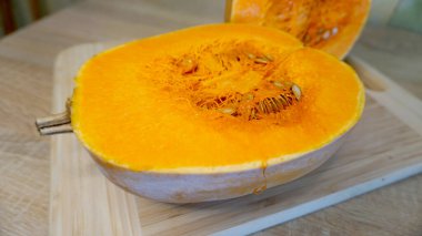 Tahta kesme tahtasının üzerinde tohumlar olan büyük çiğ balkabağı dilimi.