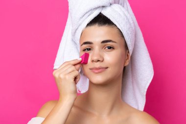 Beautiful cheerful attractive girl with a towel on her head, holds a sponge in the form of a pink heart.