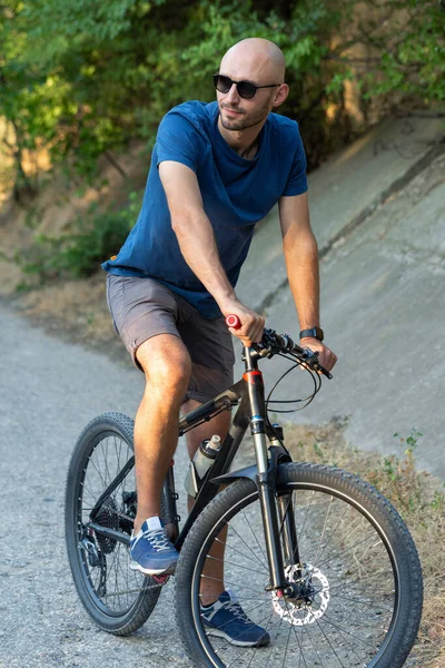 A man in casual clothes stands with a bicycle on a summer sunny day.