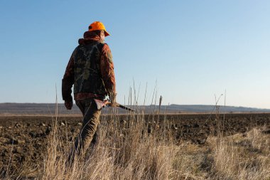 Mature man hunter with gun while walking on field.