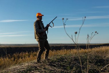 Mature man hunter with gun while walking on field.