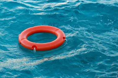 A red lifebuoy floats on the waves of the turquoise sea.