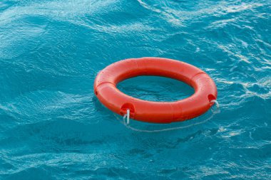 A red lifebuoy floats on the waves of the turquoise sea.