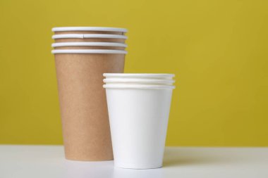 Disposable cardboard biodegradable glass on a white table, yellow background.
