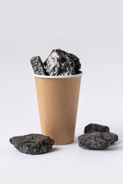 A cardboard ecological cup is filled with carbon fuel in the form of coal.