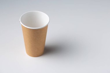 Disposable cardboard biodegradable glass on a white table, gray background.
