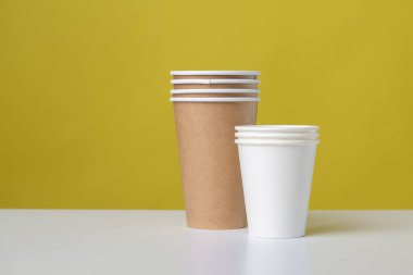 Disposable cardboard biodegradable glass on a white table, yellow background.