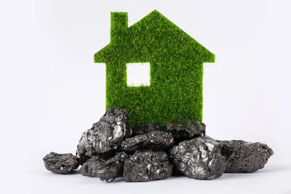 A model of a green eco house on a pile of fossil fuels in the form of coal.