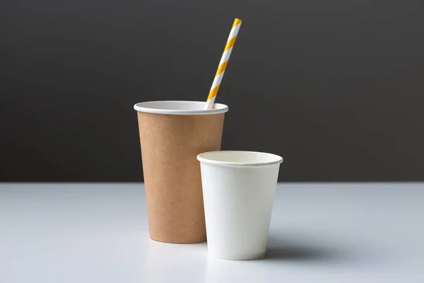 Disposable cardboard biodegradable cup on a white table with a straw.