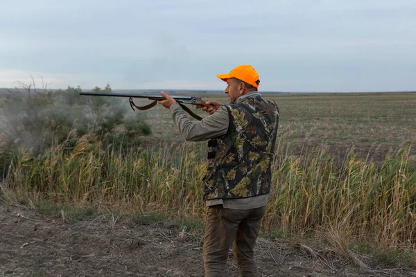 Hunter aiming with rifle while standing against sky 