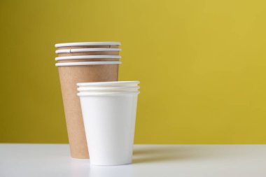 Disposable cardboard biodegradable glass on a white table, yellow background.