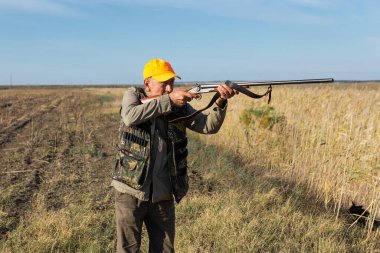 Hunter aiming with rifle while standing against sky