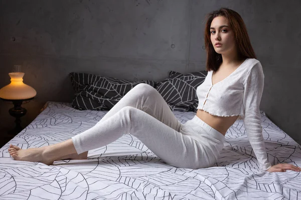 Ένα Νεαρό Ελκυστικό Κορίτσι Ντυμένο Άσπρες Πιτζάμες Αναπαύεται Ένα Κρεβάτι — Φωτογραφία Αρχείου