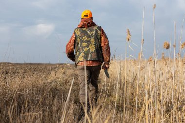Mature man hunter with gun while walking on field.