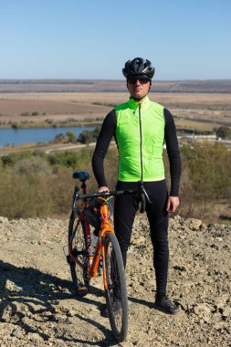 Cyclist riding bicycle on offroad against clear sky. A man in an outfit stands with a bicycle on an autumn sunny day.