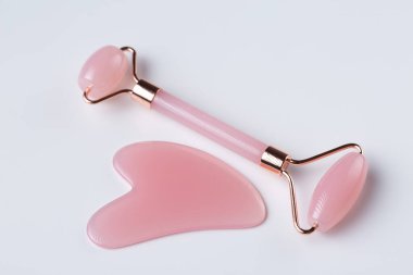 Pink Gua Sha massage tool on a white background, close-up. Rose Quartz jade roller.