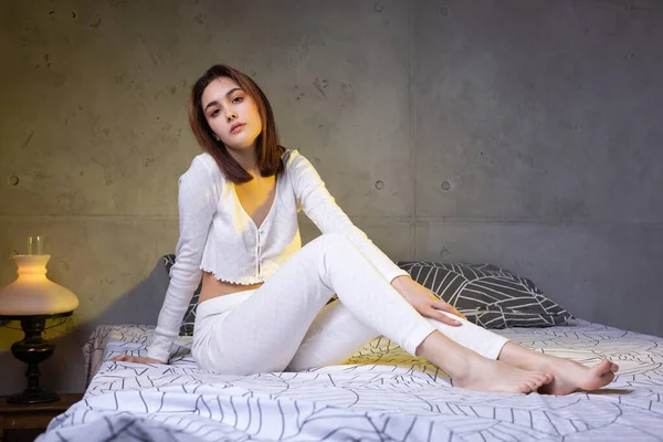 กสาวท าสนใจในช ดนอนส ขาวก อนบนเต ยงในห องนอนในแสงตอนเย — ภาพถ่ายสต็อก