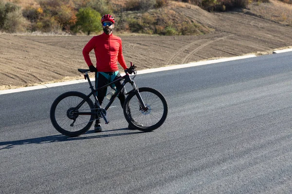 Cyclist riding bicycle on road against clear sky. A man in an outfit stands with a bicycle on an autumn sunny day.