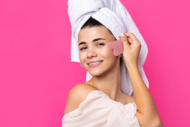 A beautiful cheerful attractive girl with a towel on her head holds a cosmetic heart stone near her face.