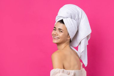 Portrait of young beautiful woman after bath. Beauty face of a cheerful attractive girl with towel on head against a pink background.