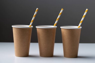 Disposable cardboard biodegradable cup on a white table with a straw.