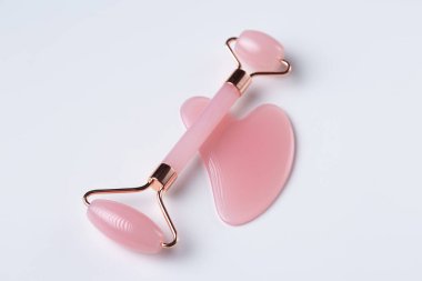 Pink Gua Sha massage tool on a white background, close-up. Rose Quartz jade roller.