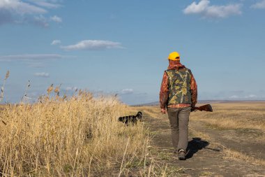 Mature man hunter with gun while walking on field.