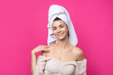 Portrait of young beautiful woman after bath. Beauty face of a cheerful attractive girl with towel on head against a pink background.