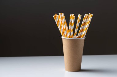 Disposable cardboard biodegradable cup on a white table with a straw.