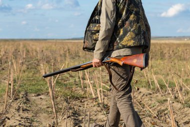 Mature man hunter with gun while walking on field.