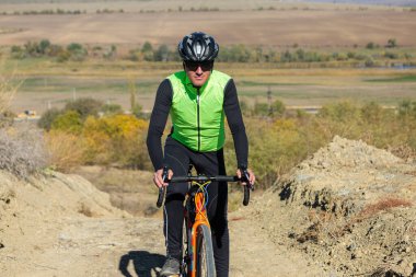 Cyclist riding bicycle on offroad against clear sky. A man in an outfit stands with a bicycle on an autumn sunny day.
