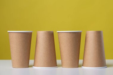 Disposable cardboard biodegradable glass on a white table, yellow background.
