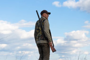 Mature man hunter with gun while walking on field.