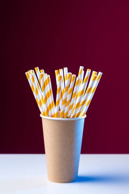 Disposable cardboard biodegradable cup on a white table with a straw against a red background.
