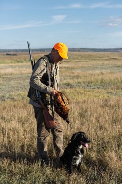 Side view of hunter carrying dead pheasant while walking on field