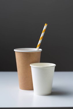 Disposable cardboard biodegradable cup on a white table with a straw.