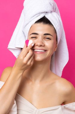 Beautiful cheerful attractive girl with a towel on her head, holds a sponge in the form of a pink heart.