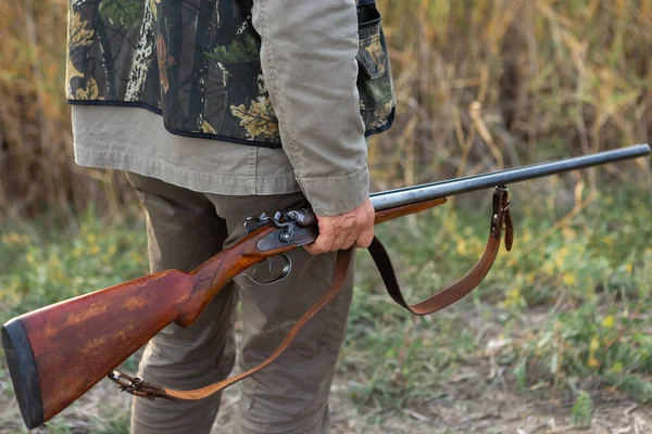 Mature man hunter with gun while walking on field.