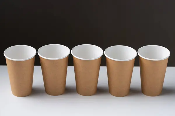 Disposable cardboard biodegradable cups on a white table, gray background.