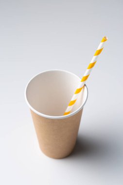 Disposable cardboard biodegradable cup on a white table with a straw.