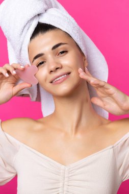 A beautiful cheerful attractive girl with a towel on her head holds a cosmetic heart stone near her face.