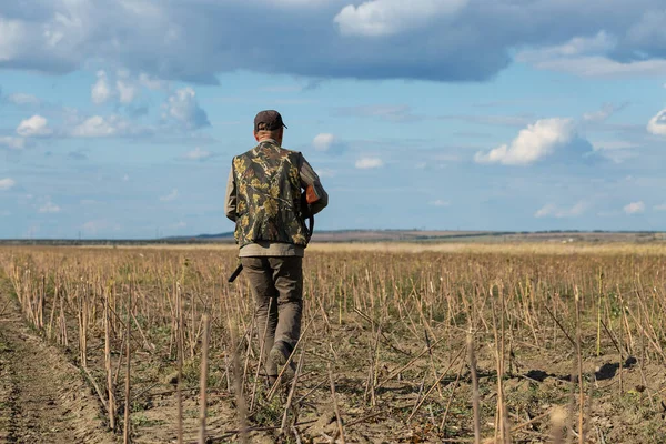 Mature man hunter with gun while walking on field.