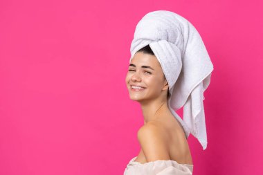 Portrait of young beautiful woman after bath. Beauty face of a cheerful attractive girl with towel on head against a pink background.