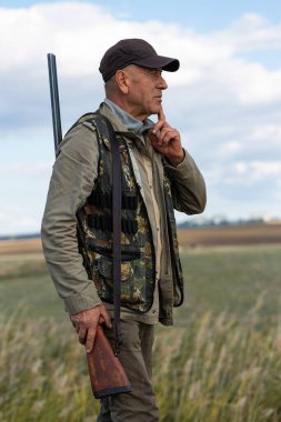 Mature man hunter with gun while walking on field.