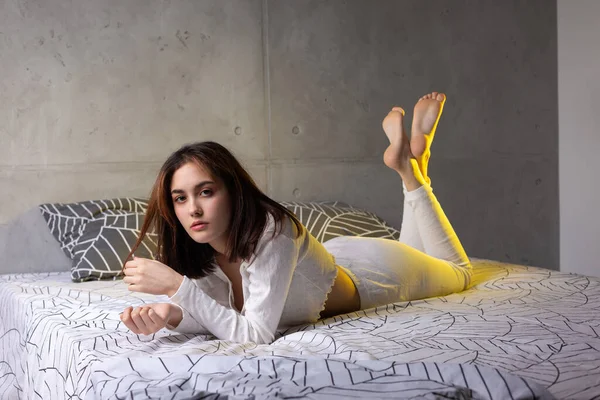 Ένα Νεαρό Ελκυστικό Κορίτσι Ντυμένο Άσπρες Πιτζάμες Αναπαύεται Ένα Κρεβάτι — Φωτογραφία Αρχείου