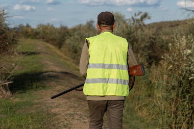 Mature man hunter with gun while walking on field.